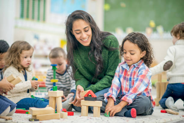 Building Together A boy and his teacher are indoors in their kindergarten classroom. They are building with blocks together. asian nanny stock pictures, royalty-free photos & images