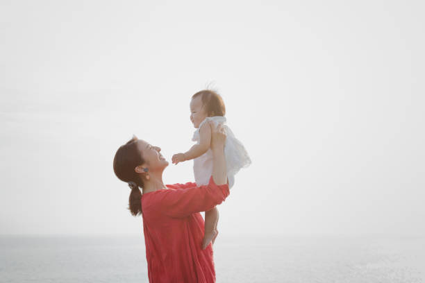 mother and baby girl relaxed at seaside - baby carrier fotos imagens e fotografias de stock