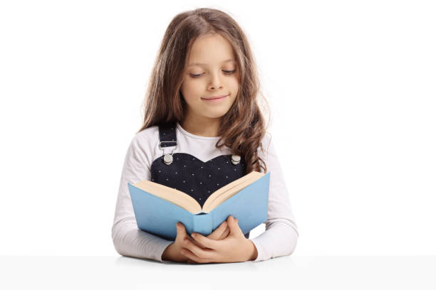 istock Little girl seated at a table reading a book 962174044