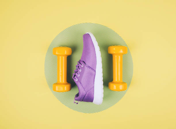 istock Orange dumbbells with a sneakeron yellow and green background 962177660