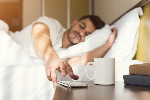 Sleepy guy waking up early after alarm clock signal Sleepy guy waking up early after hearing alarm clock signal on smartphone on monday morning, reaching for ringing mobile phone with closed eyes, copy space alarm clock snooze stock pictures, royalty-free photos & images