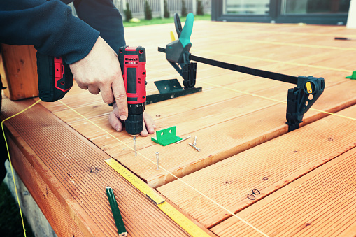 Construction worker screwing down wood deck with battery power screw gun or drill. The man screwed the terrace boards. Carpenter builds a terrace