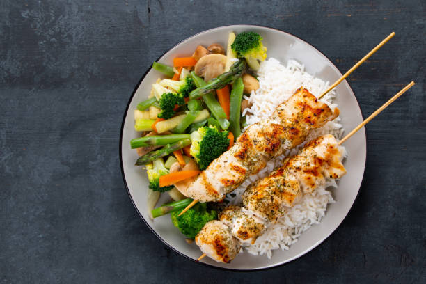Chicken skewers with steamed vegetables and long rice Grilled chicken breast skewers with steamed vegetables and long rice on a rustic blue wooden background. Top view steamed stock pictures, royalty-free photos & images