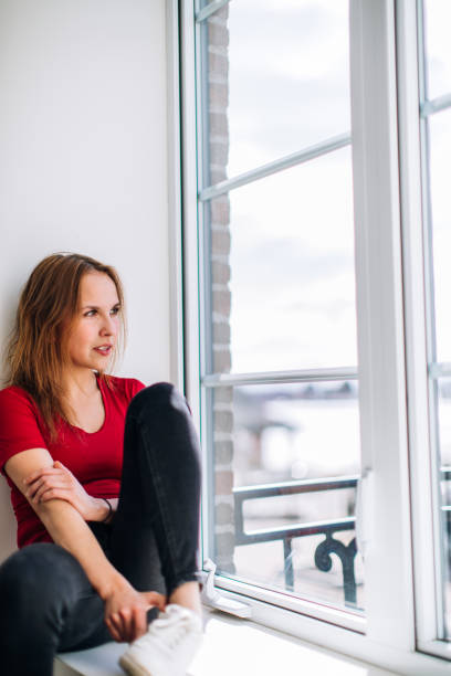 istock A young woman is sitting and looking through the window 962233470