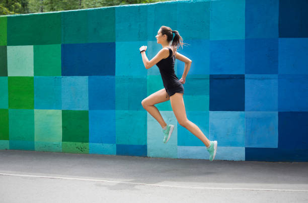 istock Side view of woman running against bright wall 962234136