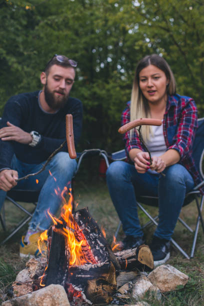 istock Happy couple fried sausages on bonfire in the forest 962235744