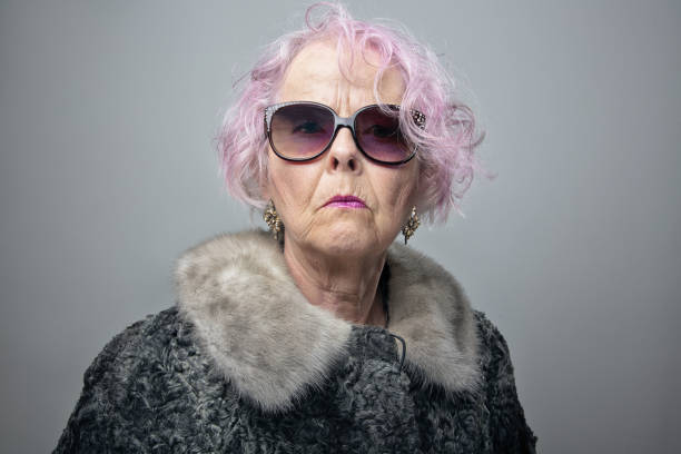 eccentric senior lady with cool attitude portrait Senior woman with pink hair wearing old fashioned fur coat and sunglasses, looking at camera with arogant expression pink hair stock pictures, royalty-free photos & images