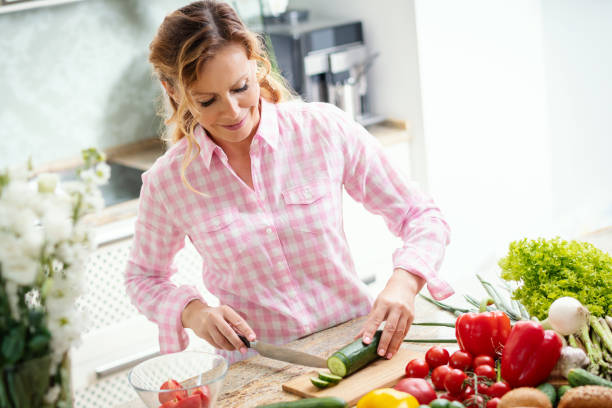 istock smiling woman is slicing cucumber on a kitchen table 962264184