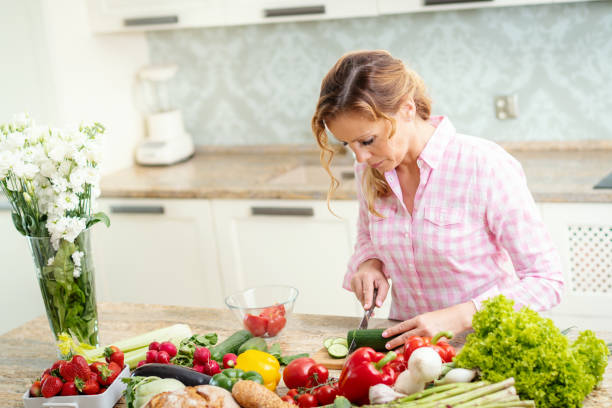 istock smiling woman is slicing cucumber on a kitchen table 962264214