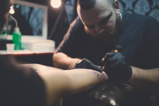 Artist making tattoo on man's hand in studio A photo of artist making tattoo on man's hand.Tattoo expert is working in studio. arm tattoo ideas for men pictures stock pictures, royalty-free photos & images
