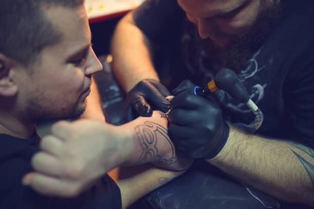 istock Tattoo artist tattooing mans forearm 962268128