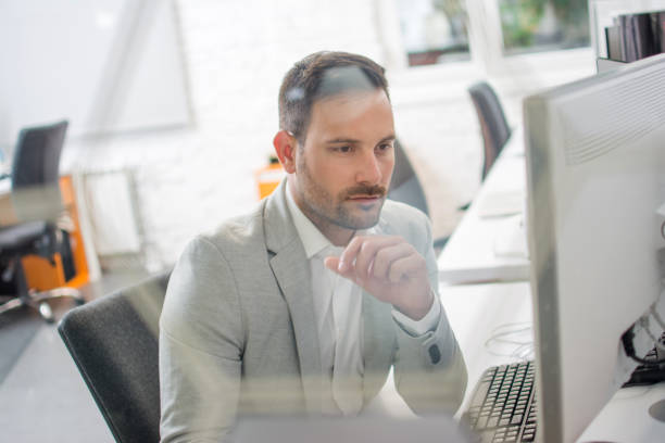 istock Through glass view of handsome man wearing formal clothes working on computer in bright office 962287718
