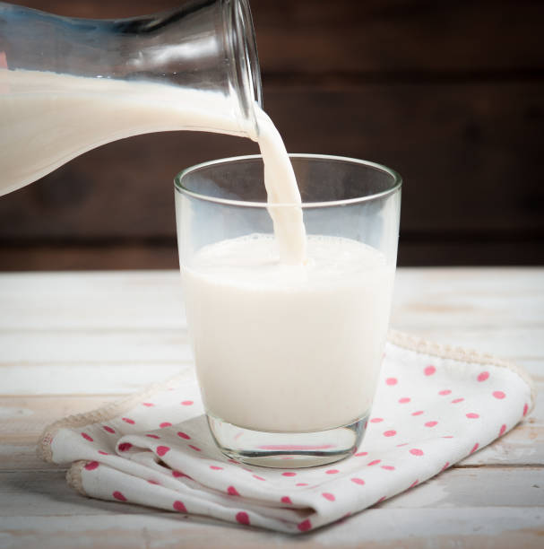 istock Milk from a jug pouring into glass on wooden 962290672