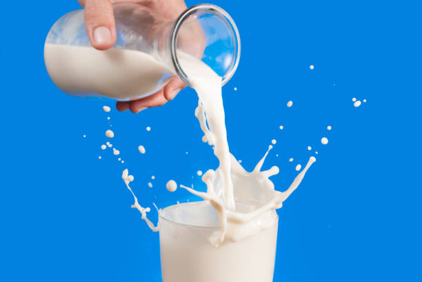istock Milk from a jug pouring into glass on a blue background 962290686