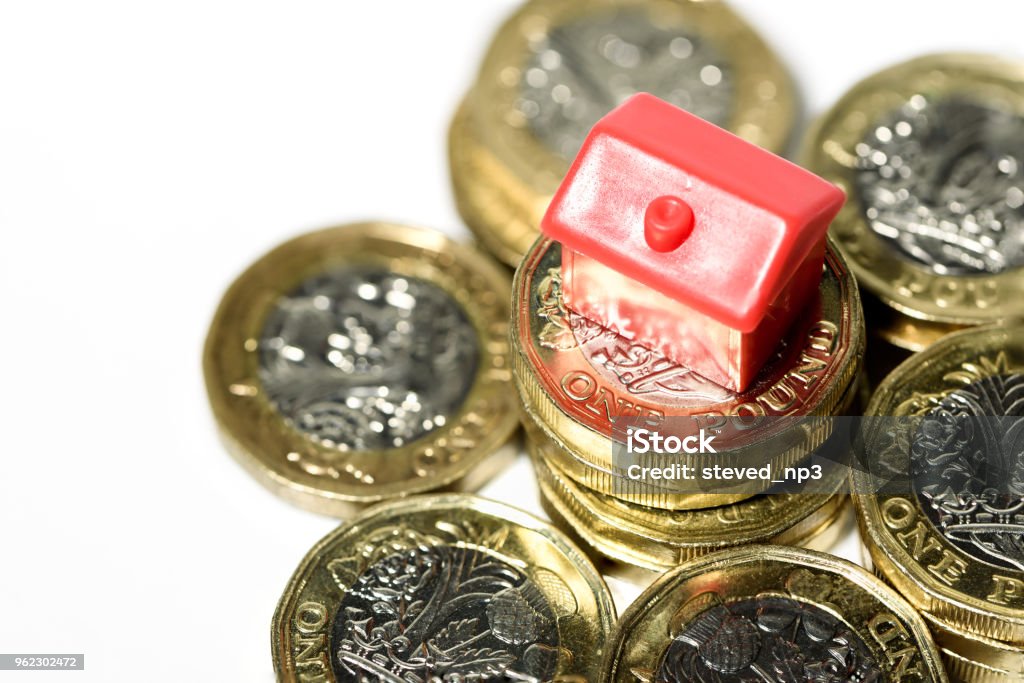 Macro close up of a Miniature house resting on new pound coins Macro close up of a Miniature house resting on new pound coins with a white background UK Stock Photo