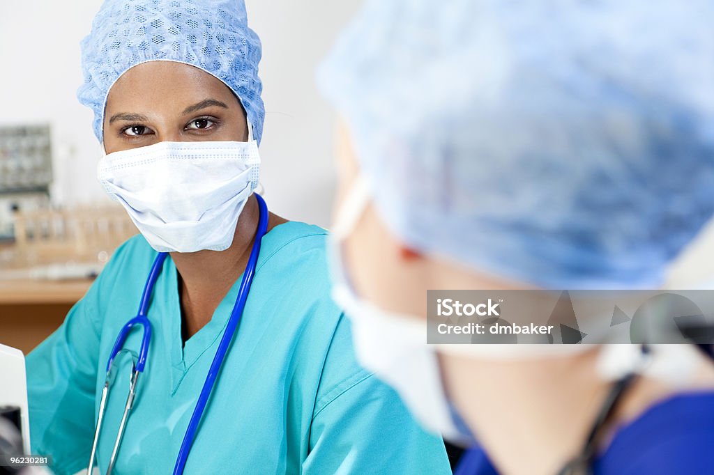 Asian Female Scientist With Her Colleague in Laboratory An Asian female medical or scientific researcher or doctor using her microscope in a laboratory and talking to her colleague out of focus in the foreground. Adult Stock Photo