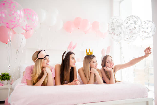 istock Cheerful, joyful, charming, pretty, funny, dreamy, cute models lying on bed shooting self portrait on front camera, holding using smart phone, having dress code, enjoying theme party 962311304