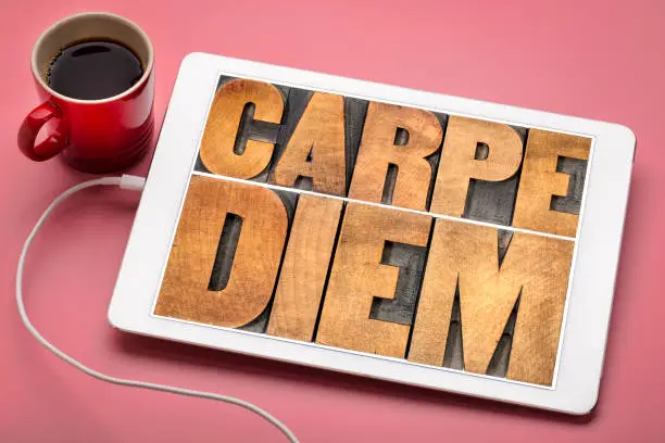 Carpe Diem  - enjoy life before it is too late, existential cautionary Latin phrase by Horace -  text in vintage letterpress wood type printing blocks on a digital tablet with a cup of coffee