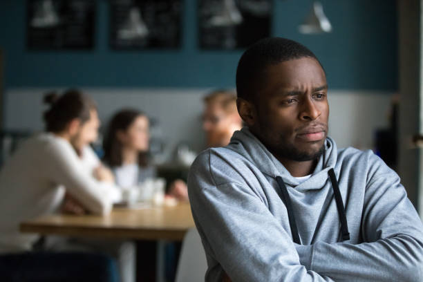 Frustrated african man suffers from racial discrimination alone in cafe Frustrated excluded outstand african american man suffers from bullying or racial discrimination having no friends sitting alone in cafe, sad depressed black guy upset being rejected by white people racism photos stock pictures, royalty-free photos & images