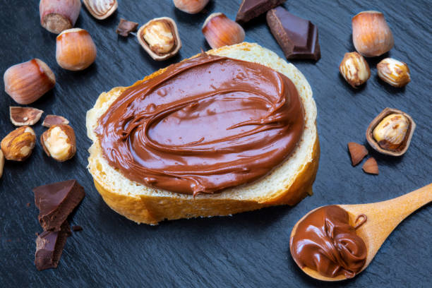 istock Slice of bread with spread chocolate cream and hazelnuts on black table 962323528