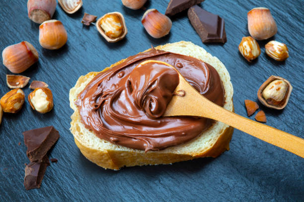 istock Slice of bread with spread chocolate cream and hazelnuts on black table 962323556