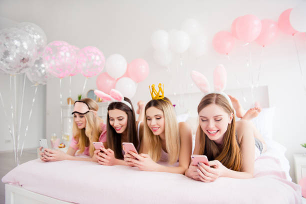 istock Cheerful, joyful, charming, pretty, funny, dreamy, cute models lying on bed having smart phone, texting sms, checking email, using wi-fi, 3G internet, wearing crown, eye-mask, bunny ears on head 962326962
