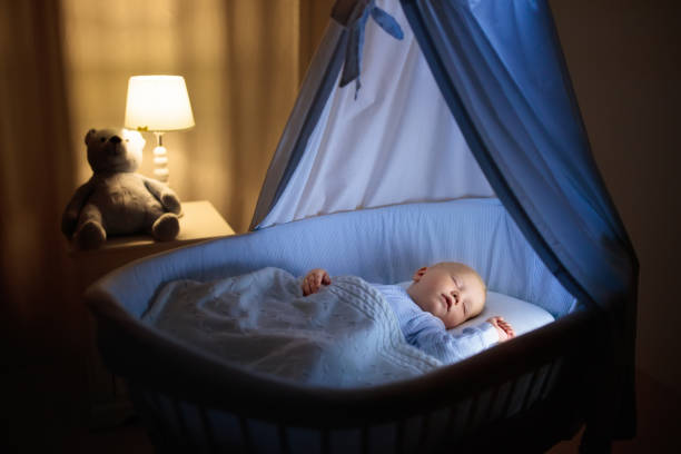 Baby boy drinking milk in bed Adorable baby drinking milk in blue bassinet with canopy at night. Little boy in pajamas with formula bottle getting ready to sleep in dark room with crib, lamp and toy bear. Bed time drink for kids. baby sleeping bedding bed stock pictures, royalty-free photos & images