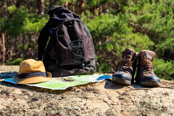 istock Tourist backpack with hiking boots, hat, compass and map on the glade in pine forest 962348578