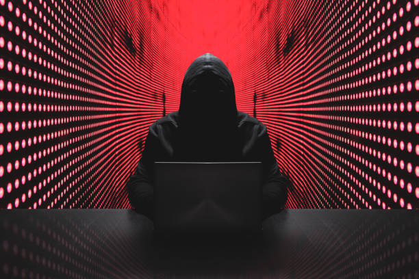 Anonymous hacker with laptop in front of binary code cyber security Anonymous hacker in front of his computer with red light wall backgroundAnonymous hacker in a black hoody with laptop in front of a code background with binary streams cyber security concept computer hacker photos stock pictures, royalty-free photos & images