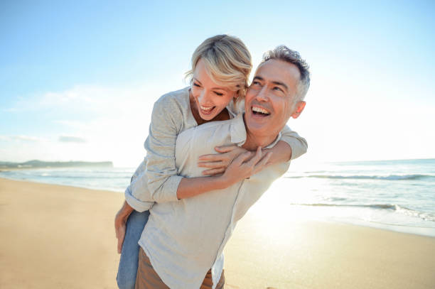 mature couple jouant sur la plage au coucher du soleil ou au lever du soleil. - beauty and health flash photos et images de collection