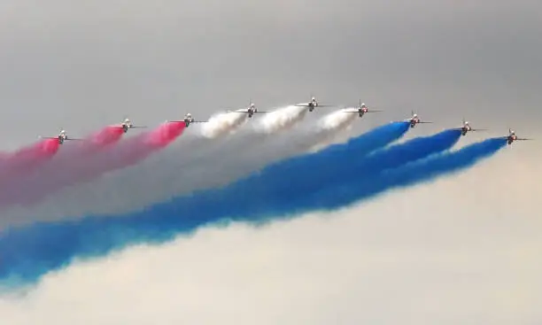 Nine Airplanes with colored smoke from their tails of red white and blue flying in formation line