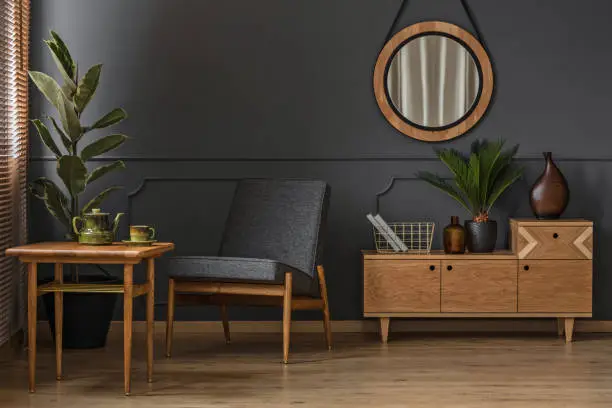 Sitting corner with wooden table, green cup and pot in a grey room interior with mirror and cabinet