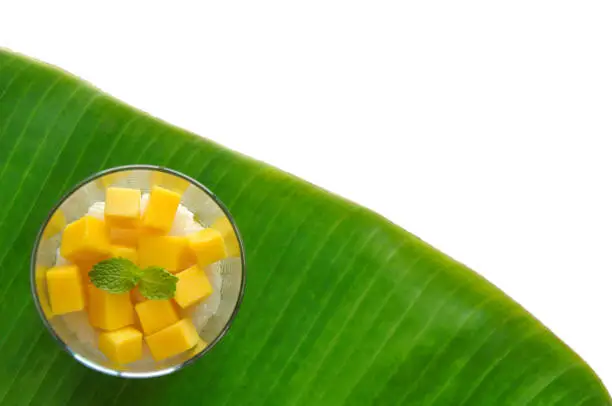 Photo of Mango sticky rice and coconut milk decorate in the glass put on banana leaf.