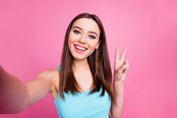 I'm selfie queen! Portrait of cute charming lovely sweet attractive tender girl with straight smooth brown hair taking self picture and presenting v-sign to subscribers, isolated on pink background I'm selfie queen! Portrait of cute charming lovely sweet attractive tender girl with straight smooth brown hair taking self picture and presenting v-sign to subscribers, isolated on pink background peace sign gesture photos stock pictures, royalty-free photos & images