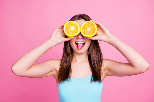 I don't see you! Portrait of amusing comic entertaining humorous laughable beautiful lovely cute pretty joke girl fooling around playing with orange slices, isolated on pink background