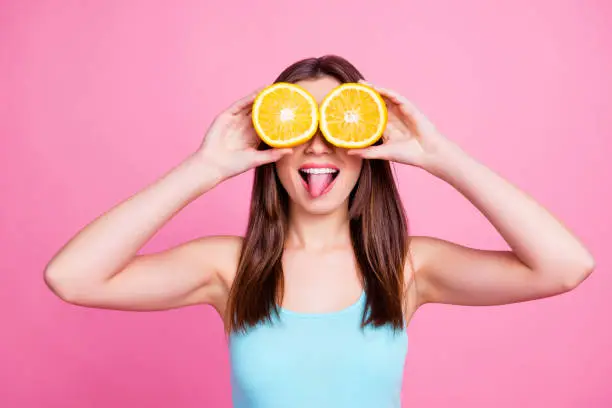 Photo of I don't see you! Portrait of amusing comic entertaining humorous laughable beautiful lovely cute pretty joke girl fooling around playing with orange slices, isolated on pink background
