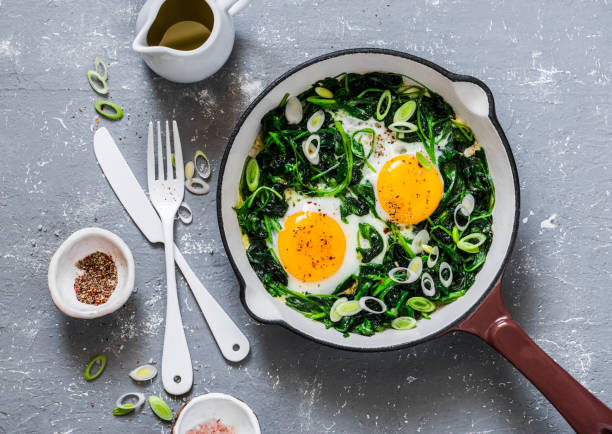 istock Green shakshuka. Fried eggs with fresh spinach, ramson, leek in a pan on a gray background, top view 962417030