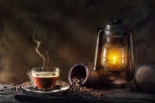 Coffee cup glass and vintage kerosene lamp oil lantern burning with glow soft light aged wood floor