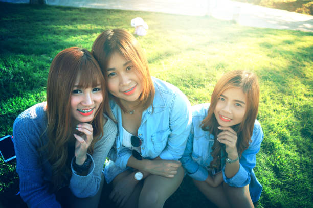 three asia smile girl spending free time, sitting on the grass in the park, relaxing