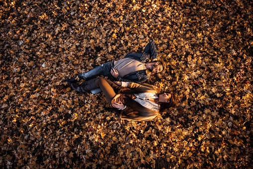 High angle view of relaxed couple enjoying a day in autumn while lying in leaves and communicating. Copy space.