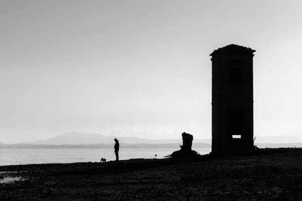 un homme marchant un chien sur une rive du lac, sous un ciel grand, vide, un - pets water lake sky photos et images de collection