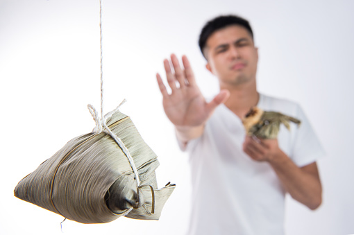 A man feels sick after eating too much delicious zongzi(rice dumpling) and saying never eat again on Dragon Boat Festival, Asian traditional food, white background