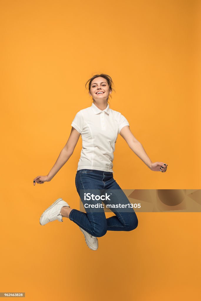 Freedom in moving. Pretty young woman jumping against orange background Freedom in moving. Mid-air shot of pretty happy young woman jumping and gesturing against orange studio background. Runnin girl in motion or movement. Human emotions and facial expressions concept Women Stock Photo