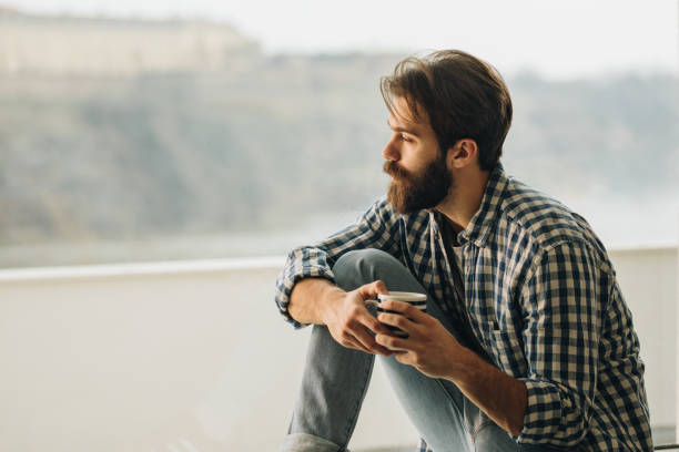 istock Young man sitting by the window during his coffee time and looking through it. 962464260