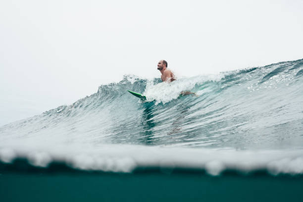 istock handsome young man with surfboard on top of ocean wave 962473198