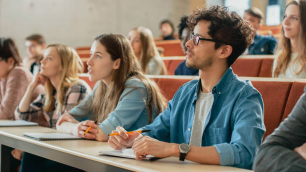 in classe studenti multietnici che ascoltano un docente e scrivono in quaderni. i giovani intelligenti studiano al college. - istruzione post secondaria foto e immagini stock