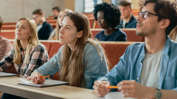 istock In the Classroom Multi Ethnic Students Listening to a Lecturer and Writing in Notebooks. Smart Young People Study at the College. 962475728