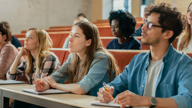 istock In the Classroom Multi Ethnic Students Listening to a Lecturer and Writing in Notebooks. Smart Young People Study at the College. 962475730