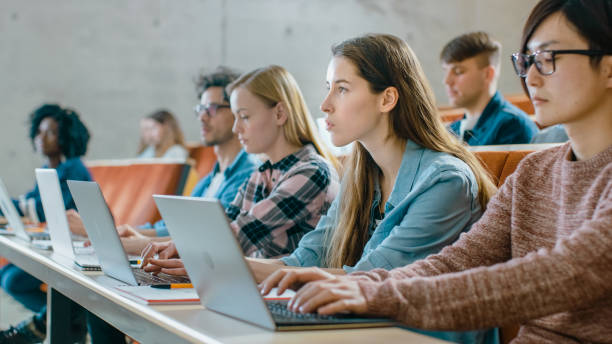 istock Large Group of Multi Ethnic Students Working on the Laptops while Listening to a Lecture in the Modern Classroom. Bright Young People Study at University. 962475944