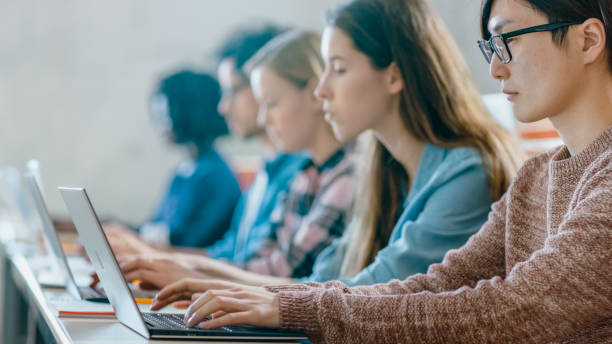 istock Row of Multi Ethnic Students Working on the Laptops while Listening to a Lecture in the Modern Classroom. Bright Young People Study at University. 962475954